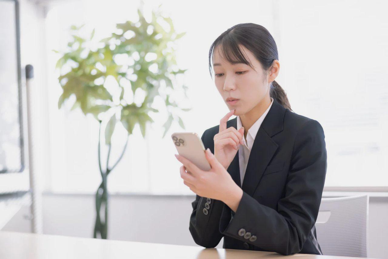 スマートフォンを操作する手と、コーヒーカップとノートが置かれたカフェのテーブル